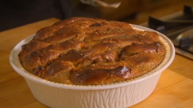 A golden-brown, freshly baked pie with a criss-crossed crust sits in a white ceramic dish on a wooden worktop near a cooker, reminiscent of the comforting classics found in the Best of British Cookbook.