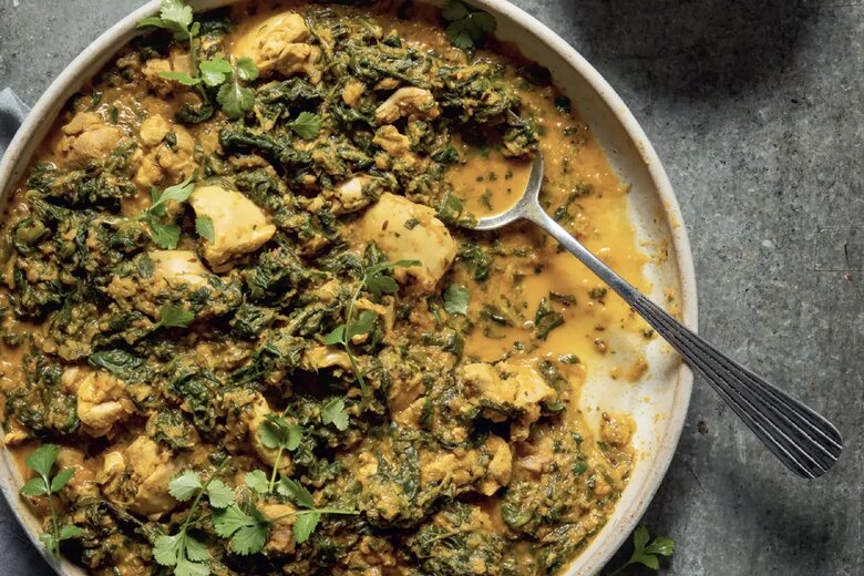 A bowl of Chicken &amp; Spinach Curry, with tender chicken and spinach in a creamy sauce, is garnished with coriander. Inspired by Hairy Dieters Simple Healthy Food, it’s served with yoghurt on the side atop a grey surface.