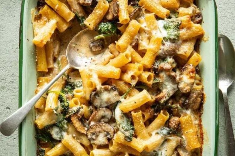 This dish is one of our family favourites: creamy pasta bake with mushrooms, spinach, and cheese in a rectangular dish, served with a silver spoon.