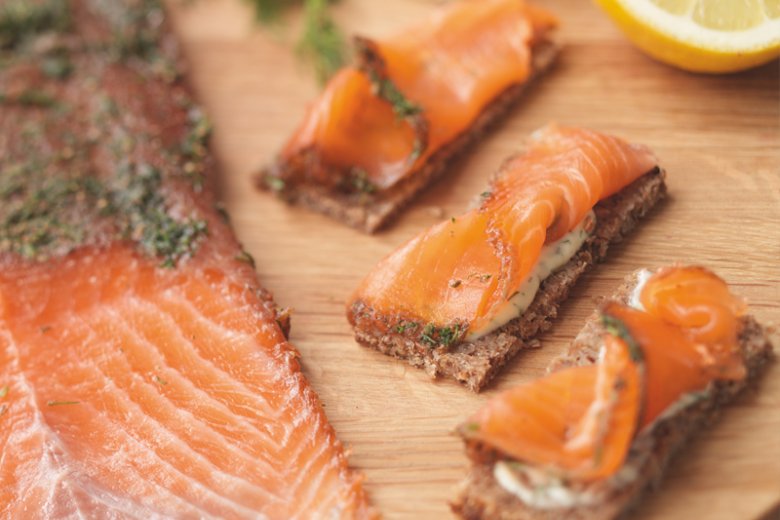 Slices of cured salmon on a wooden board, with three pieces of rye bread topped with festive Christmas gravlax and herbs. A lemon half and some herbs are visible in the background, inspired by Hairy Bikers 12 Days of Christmas.