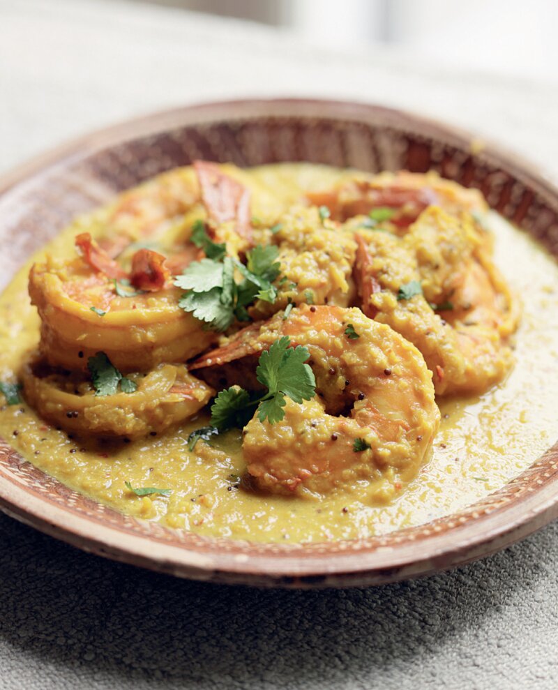 A plate of shrimp in a yellow curry sauce, inspired by a Keralan King Prawn Curry, garnished with fresh coriander