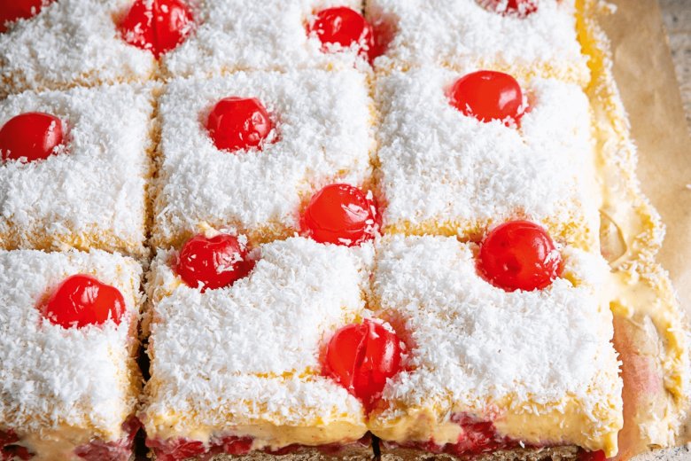 Nine square slices of Manchester Tart Flapjack, topped with shredded coconut and red cherries, are arranged on parchment paper—truly Everyday Winners for any dessert table.