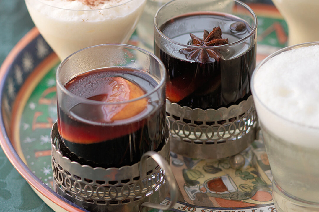 Two glass cups of dark mulled wine, garnished with orange slices and star anise, sit in ornate metal holders on a colourful tray—Indulge in the Best-Ever Mulled Wine Recipe from the Hairy Bikers beside other creamy drinks.