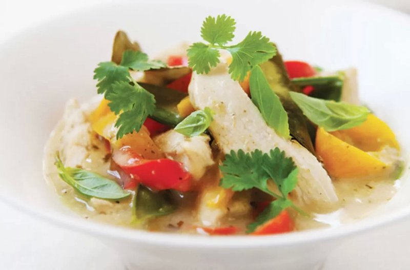A white bowl filled with Thai Chicken and Coconut curry, featuring pieces of chicken, red and yellow peppers, green beans, and fresh herbs like coriander and basil, all in a creamy, light green sauce inspired by a Hairy Bikers recipe.