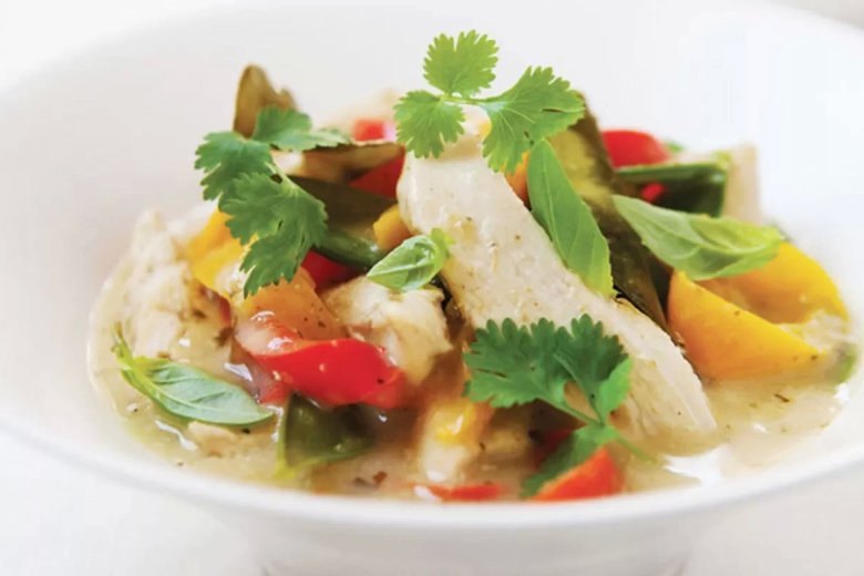 A white bowl filled with Thai Chicken and Coconut curry, featuring pieces of chicken, red and yellow peppers, green beans, and fresh herbs like coriander and basil, all in a creamy, light green sauce inspired by a Hairy Bikers recipe.