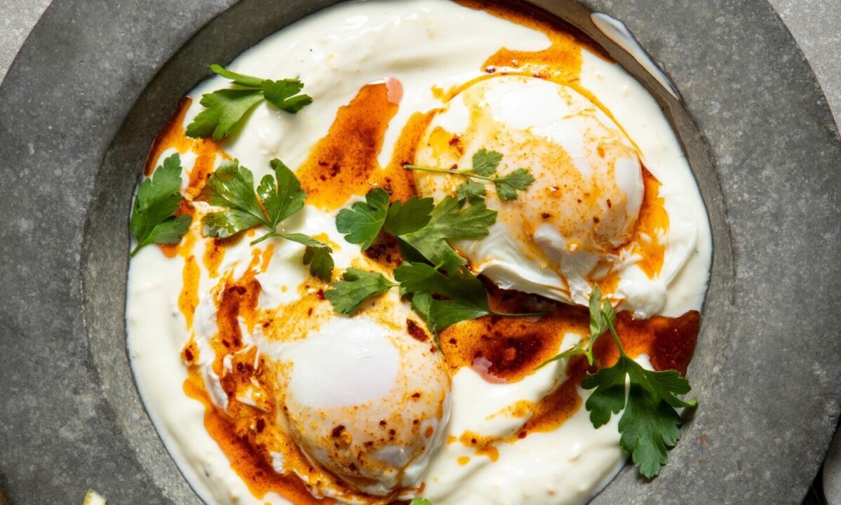 A plate of Turkish eggs with two poached eggs on a bed of yogurt, drizzled with chili-infused oil and garnished with fresh parsley, straight from the Hairy Dieters' Simple Healthy Food collection.