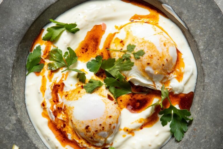 A plate of Turkish eggs with two poached eggs on a bed of yogurt, drizzled with chili-infused oil and garnished with fresh parsley, straight from the Hairy Dieters' Simple Healthy Food collection.